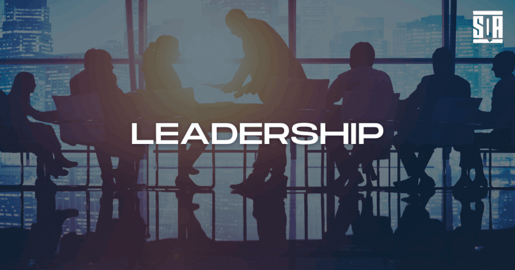 SQA Services’ leadership figures standing outdoors near a scenic oceanfront cliff, dressed in suits, with the word “HISTORY” prominently displayed—symbolizing the company’s legacy and founding story.